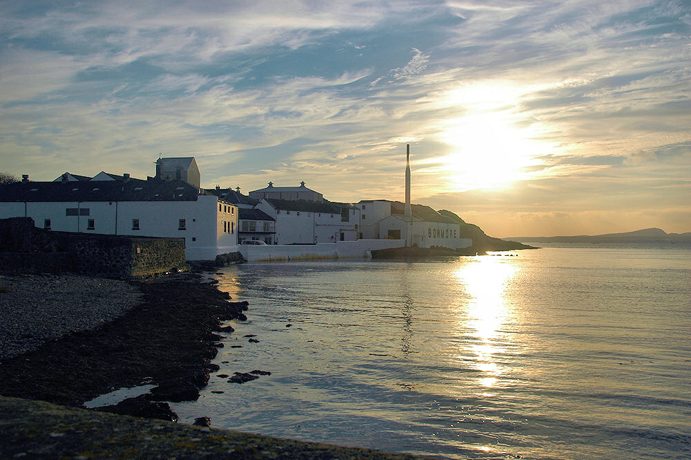 Picture of a hazy sun seen from the pier in a coastal village with a whisky distillery