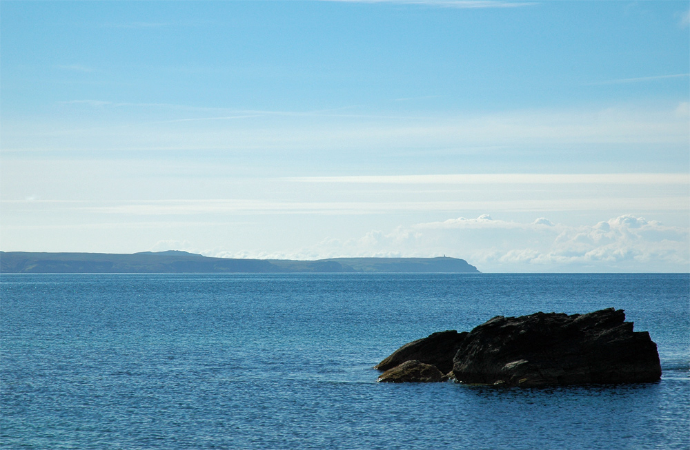 Picture of the Mull of Oa seen across Loch Indaal, a rock in the foreground