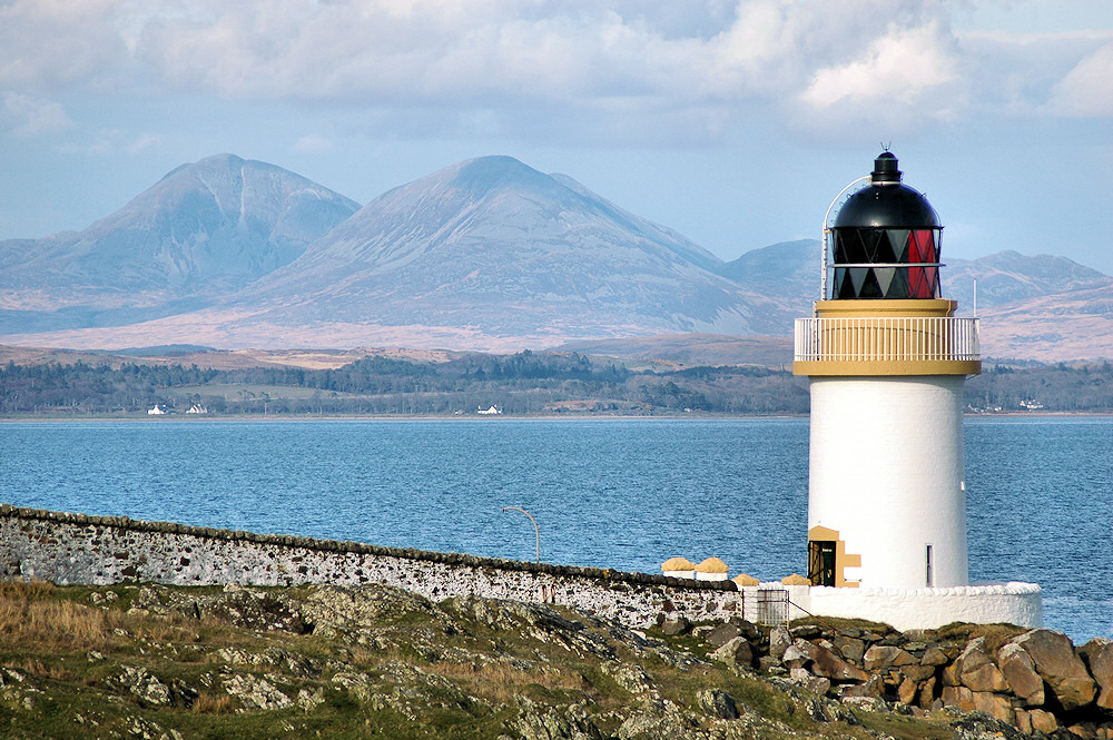 Picture of a small lighthouse with a sea loch and mountains in the background