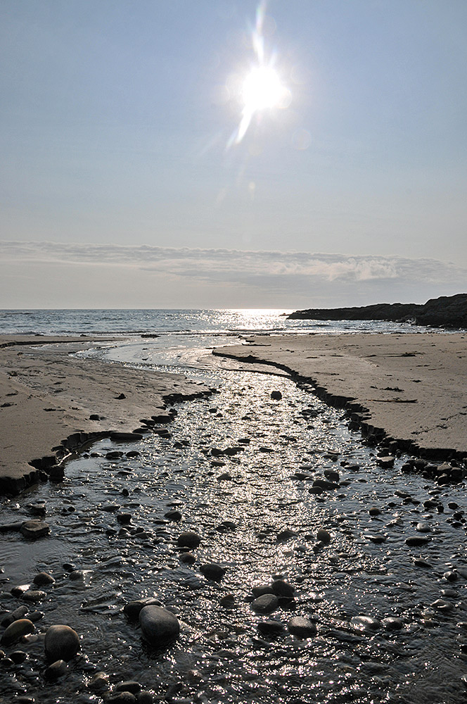 Picture of the evening sun reflecting in a burn running over a west facing small beach