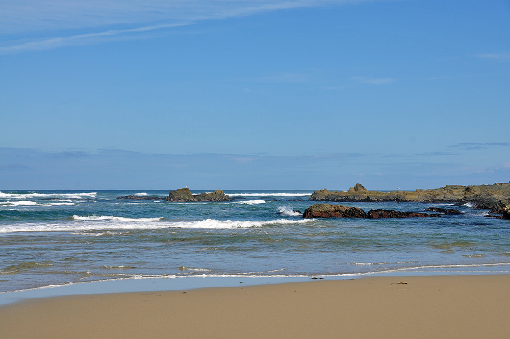 Picture of a beach with some offshore rocks, small waves breaking