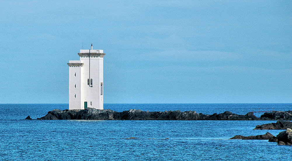 Picture of a white square lighthouse on a rocky outcrop