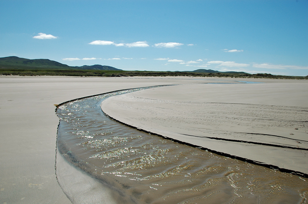 Picture of a small river running across a wide sandy beach