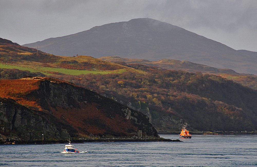 Picture of a view along a sound, a lifeboat anchored and a small fishing boat cruising