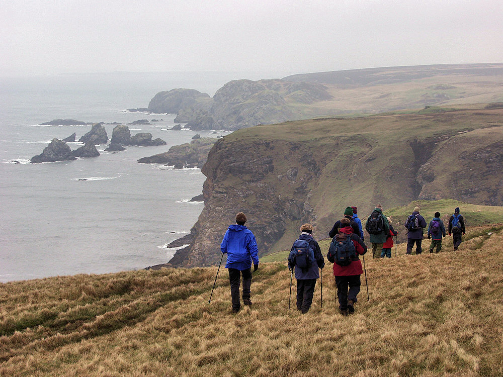 Picture of a group of walkers on rugged landscape with steep cliffs over the sea