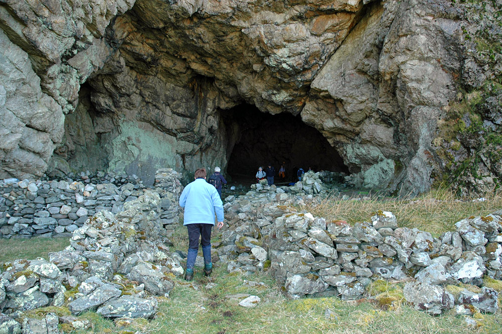 Picture of a large cave in a cliff face, several people walking around in the entrance