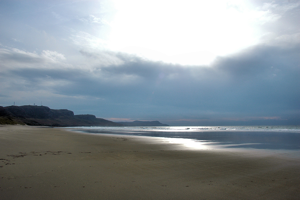Picture of heavy clouds as well as bright sun over a bay with a wide sandy beach