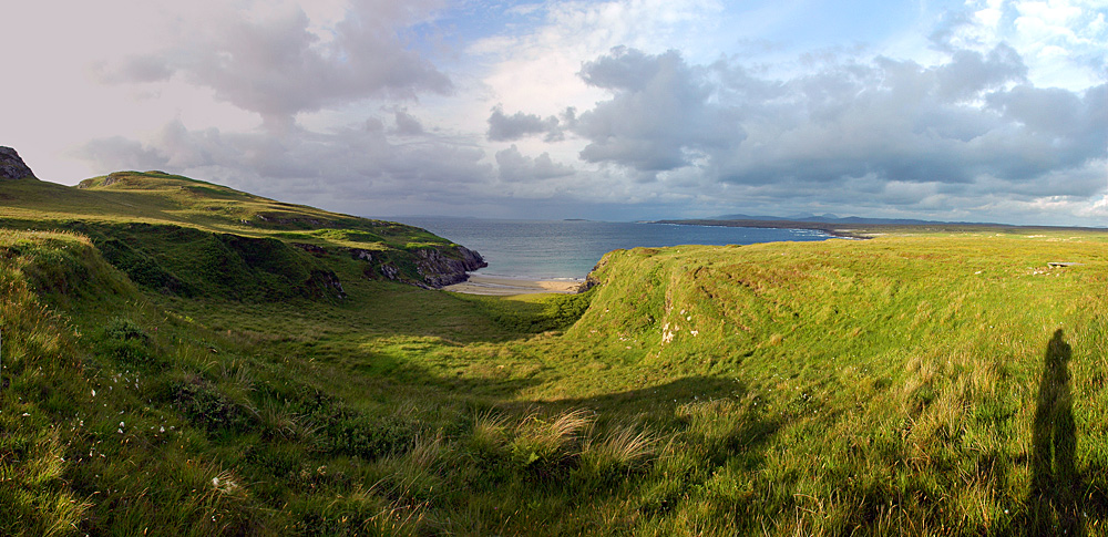 Panoramic picture of a view over a north facing coast with a small beach. Clouds ahead but sun from behind
