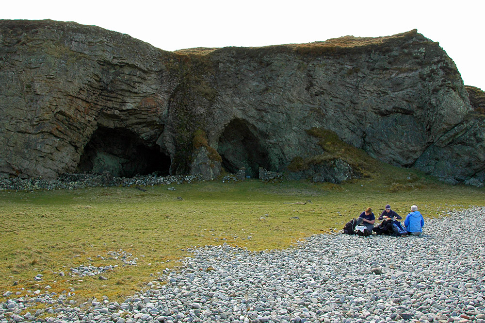 Picture of three women sitting outside two large caves in a cliff face