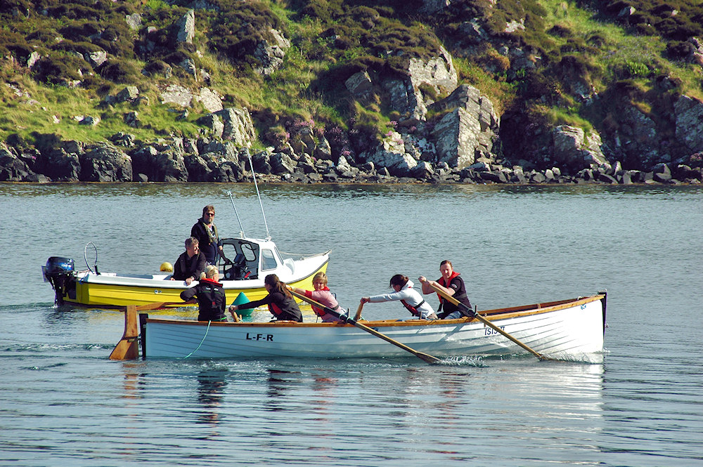 Picture of people rowing a skiff under the watchful eyes of their coach