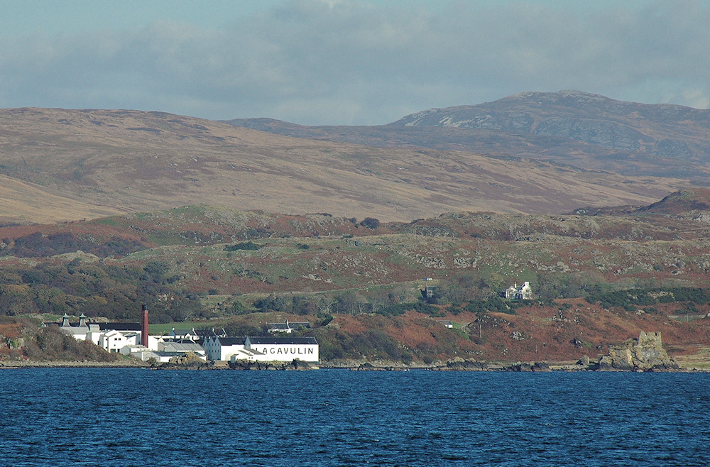 Picture of a coastal distillery and the ruin of a castle seen from a passing ferry