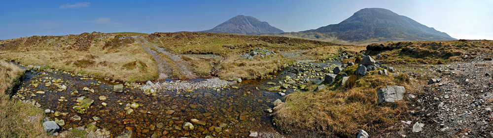 Picture of a panoramic view of a burn crossing a track below two mountains