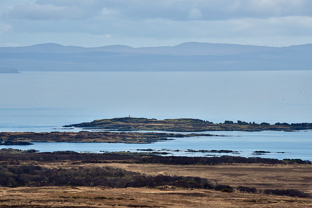 Picture of skerries on a coast seen from an inland hill on an island, the mainland in the distance