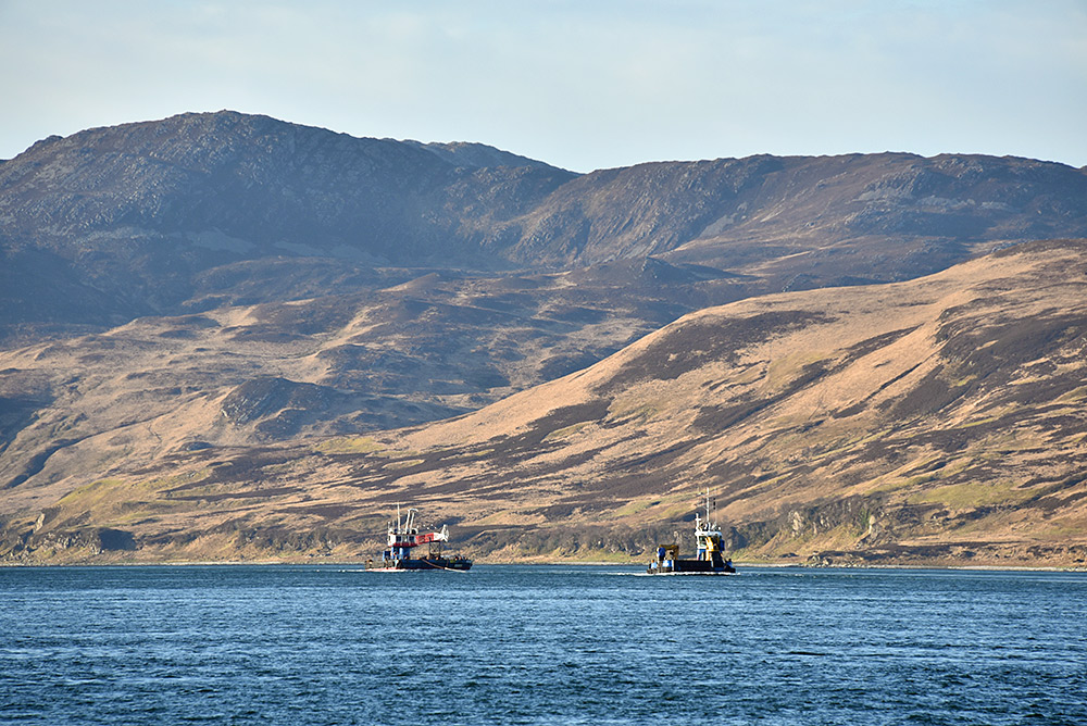 Picture of a barge towing a crane in a sound between two islands
