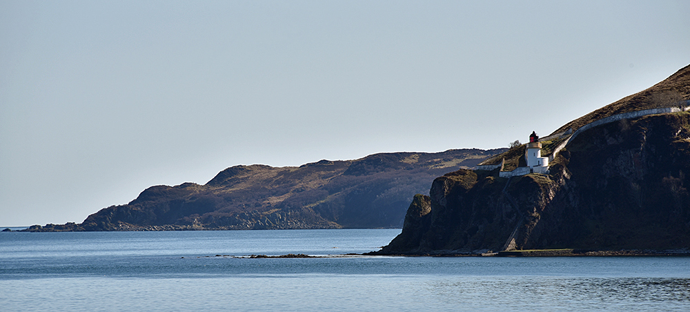 Picture of a rugged coast with a lighthouse on the top of cliffs on one side