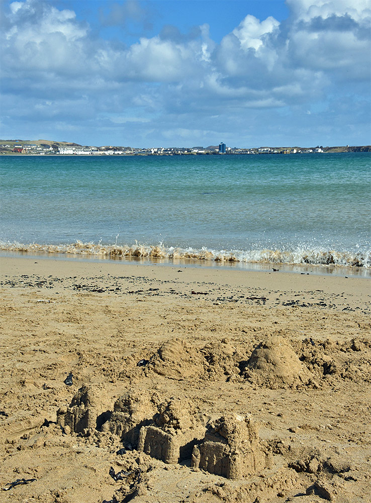 Picture of a sandcastle on a beach, a village in the distance across a bay