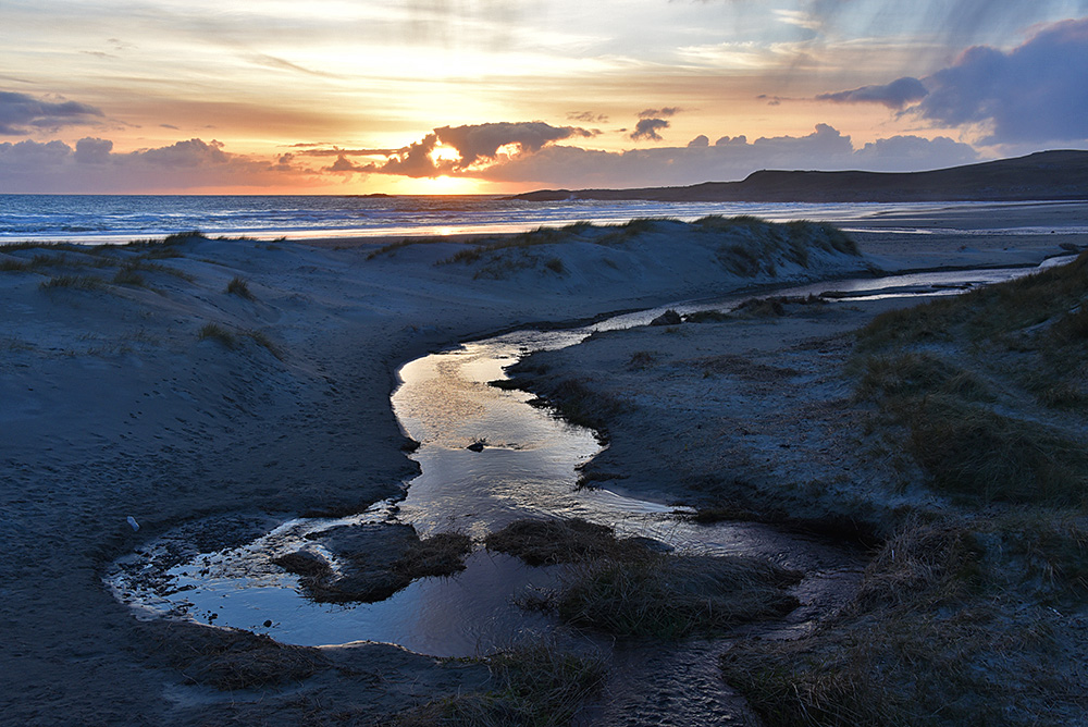 Picture of a sunset at a burn (river) running over a beach into the sea