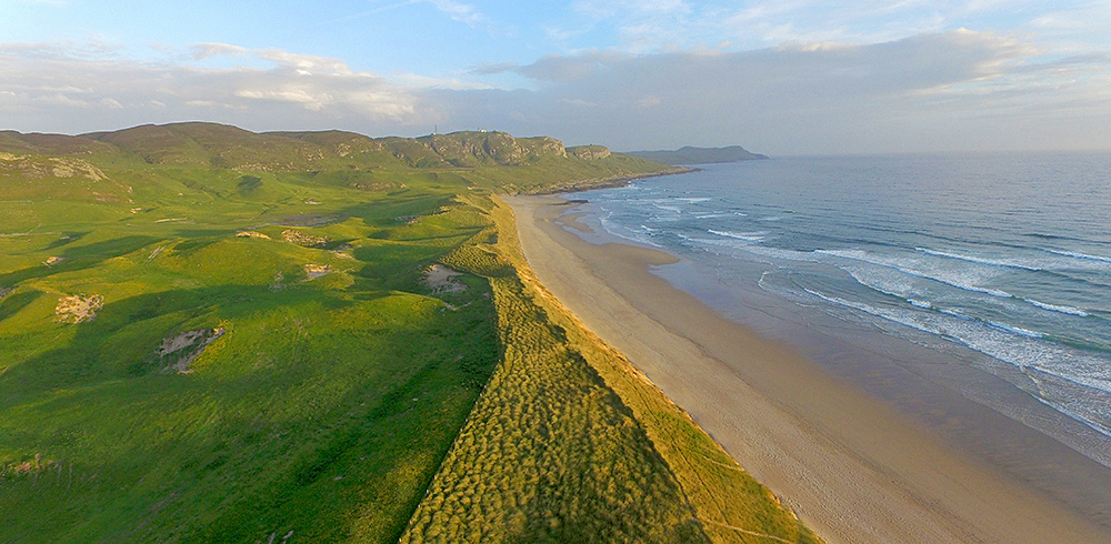 Panoramic picture of a view over dunes and a beach at a bay from the air