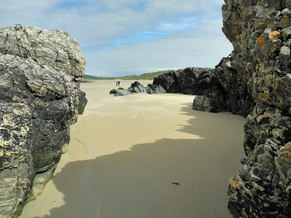 Picture of two walkers on a beach seen through rocks