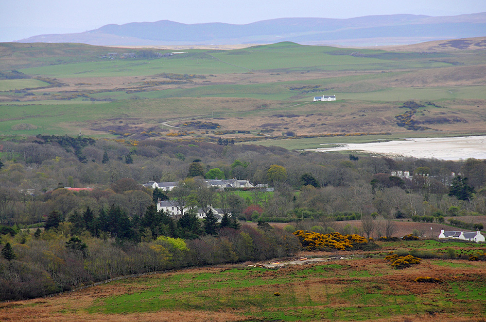 Picture of a view from a hill over various buildings surrounded by woodlands