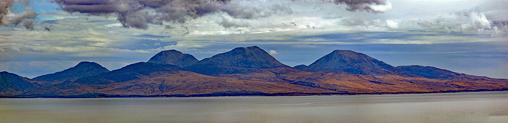 Panoramic picture of three mountains on an island seen across the sea