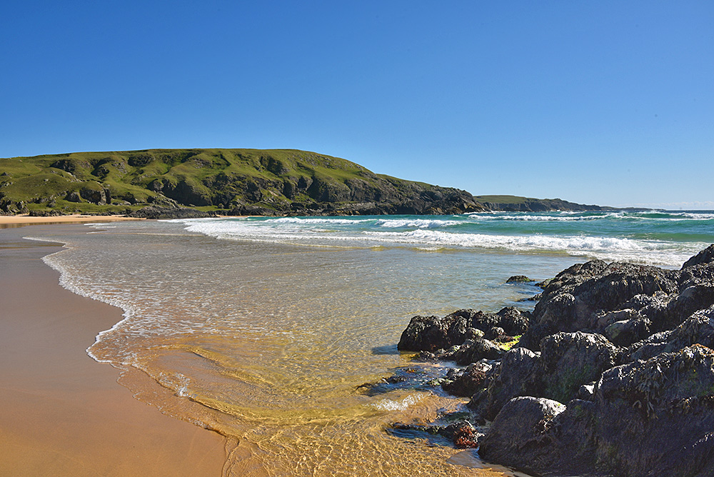 Picture of a golden sandy beach in a bay with waves rolling in on a sunny day