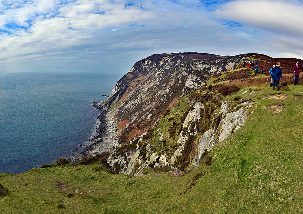 Panoramic picture of a group of walkers walking along steep cliffs above the sea