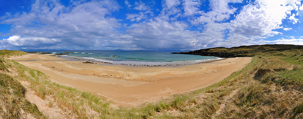 Panoramic picture of a small beach with golden sands on an island, other islands and the mainland visible in the distance