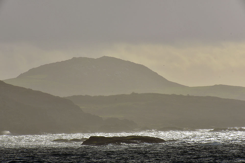 Picture of the silhouettes of hills on a small island, seen from a passing ferry