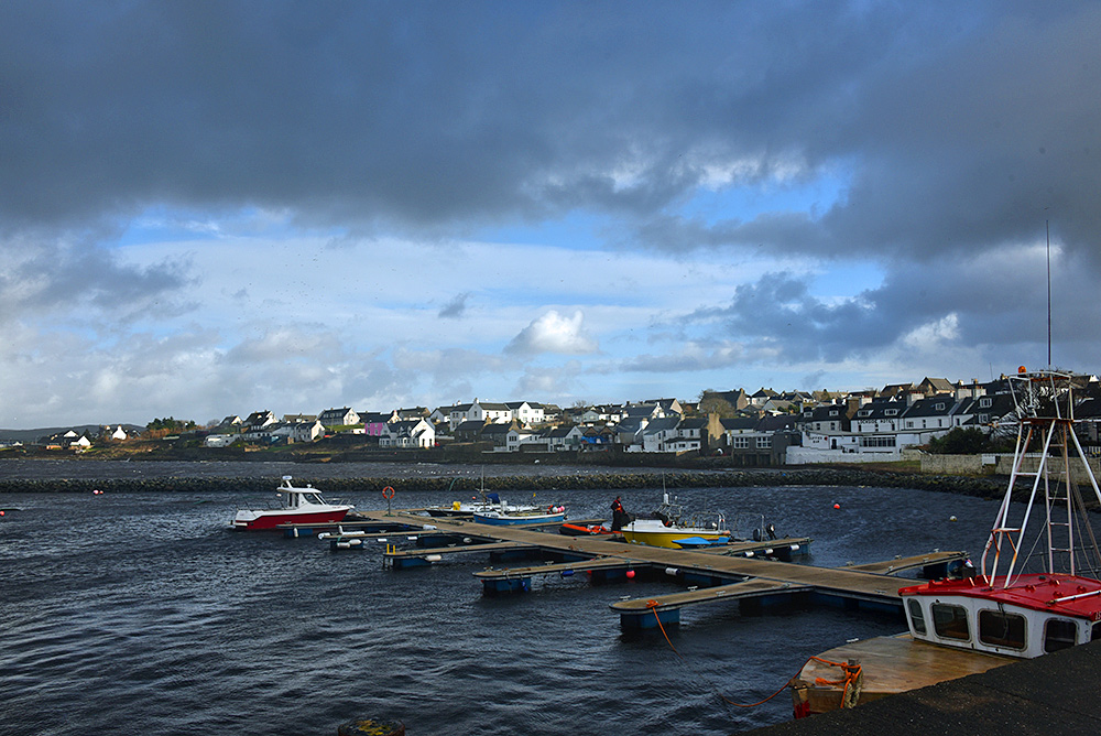 Picture of a small boat harbour next to a village, heavy clouds moving in