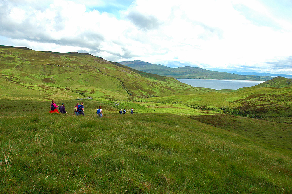 Picture of a small group of walkers descending into a glen (valley) leading to a sound between two islands