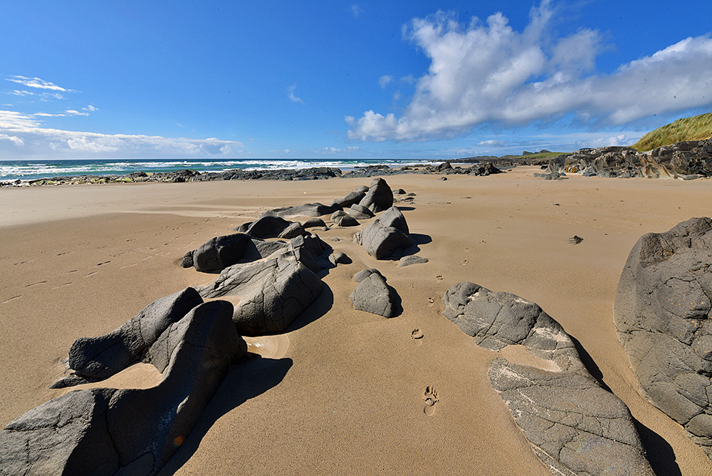 Picture of a beach with sand and rocks, some footprints in the sand