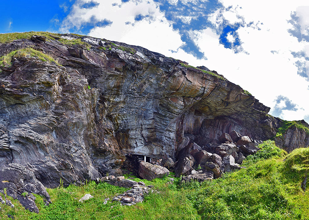 Panoramic picture of a hut under an overhanging steep cliff