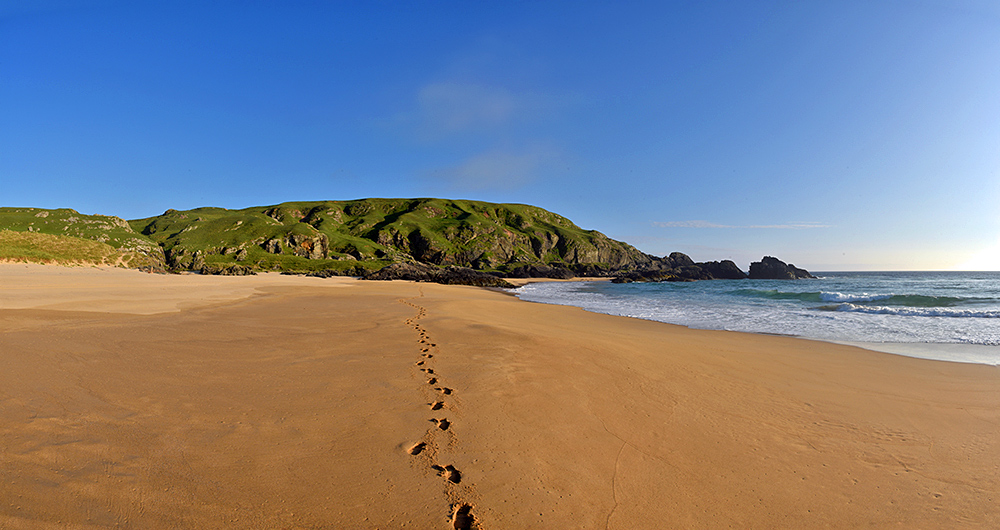 Panoramic picture of a wide sandy beach with footprints going down the middle