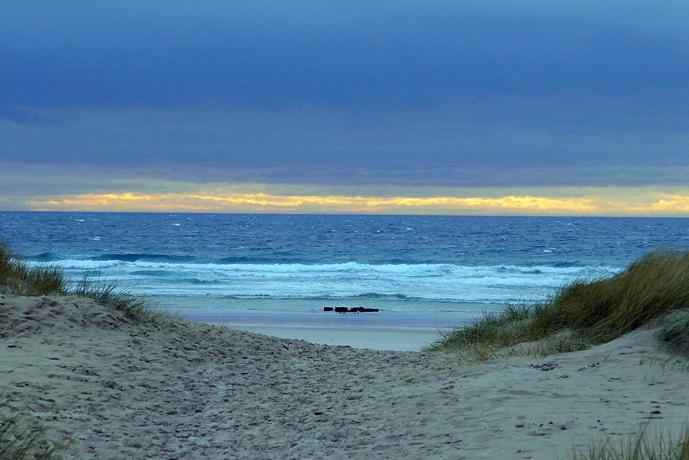 Picture of a path through dunes to a beach, clouds overhead but brighter at the horizon
