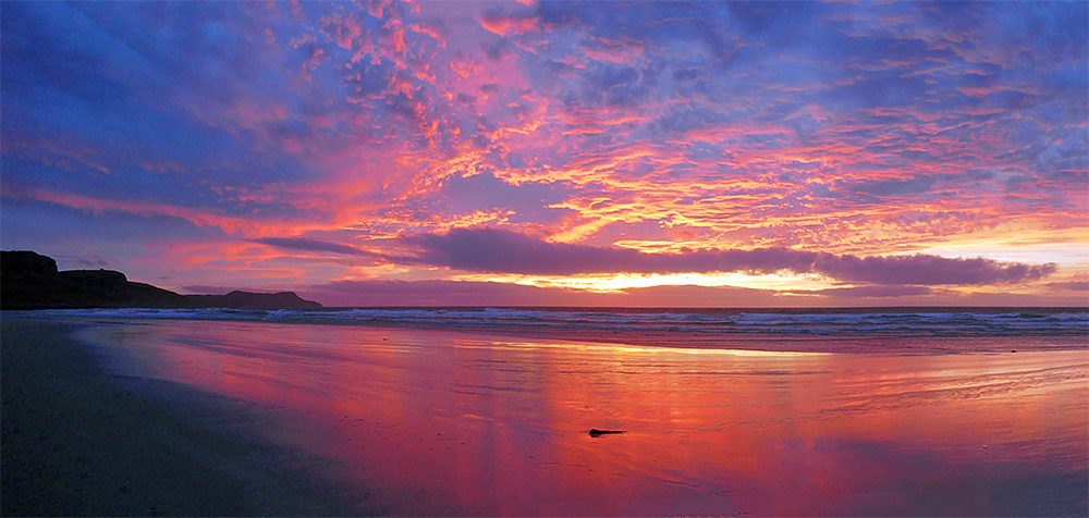 Panoramic picture of a very colourful November sunset at a bay with a sandy beach