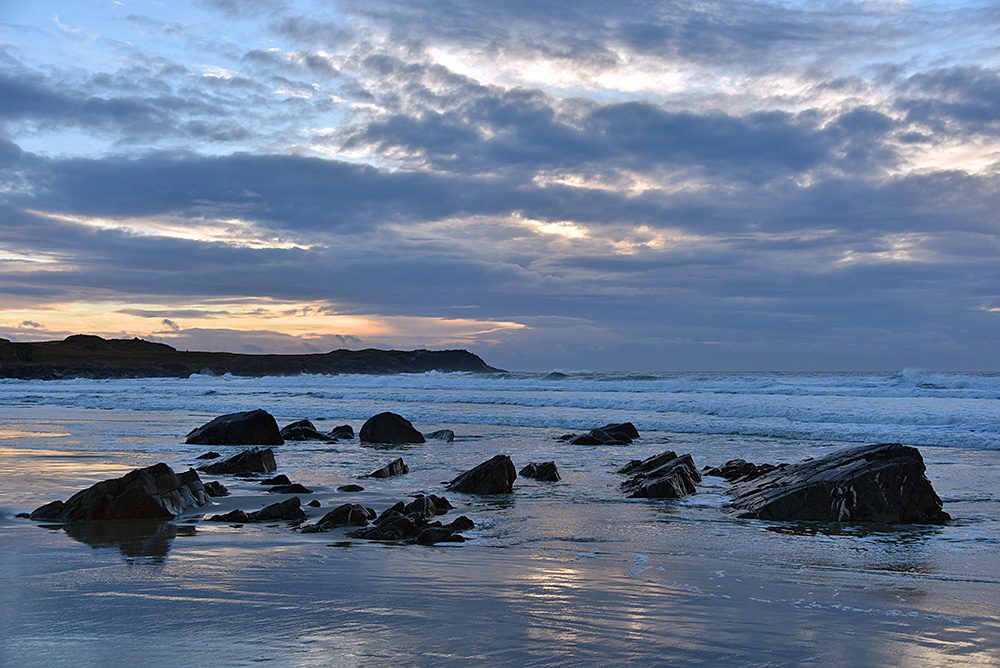 Picture of a beach with a few rocks in the sand in some mild November afternoon light under a mostly cloudy sky