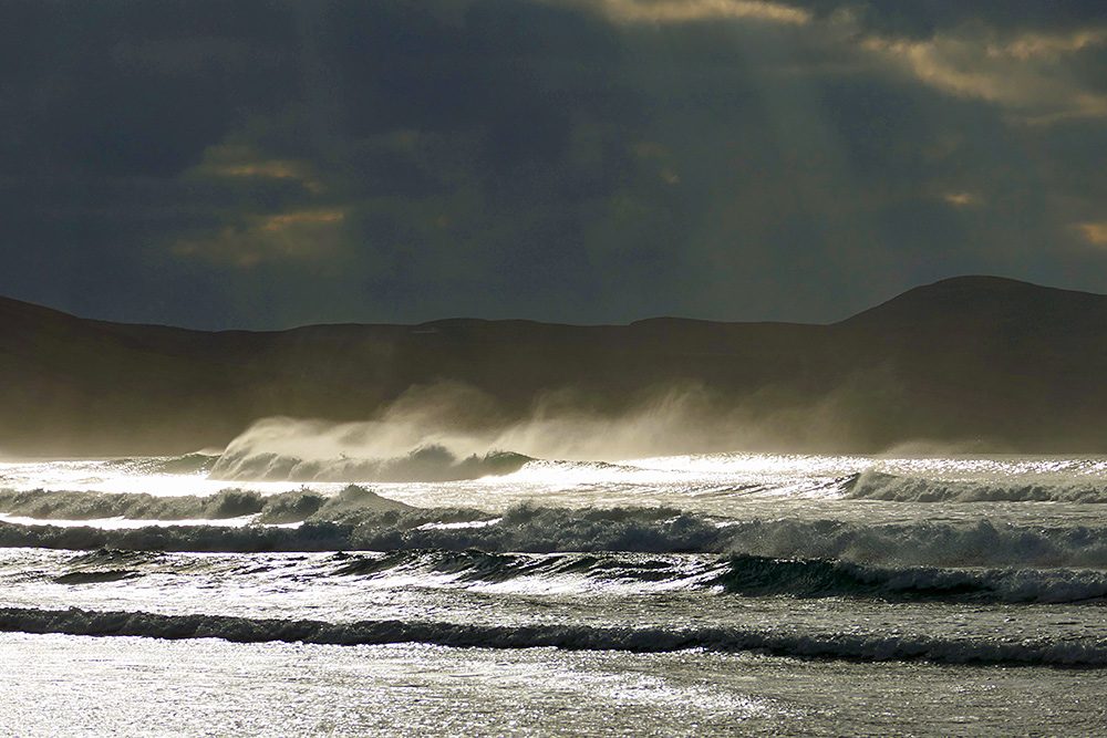 Picture of spray being blown in the air from breaking waves. illuminated by sun breaking through clouds