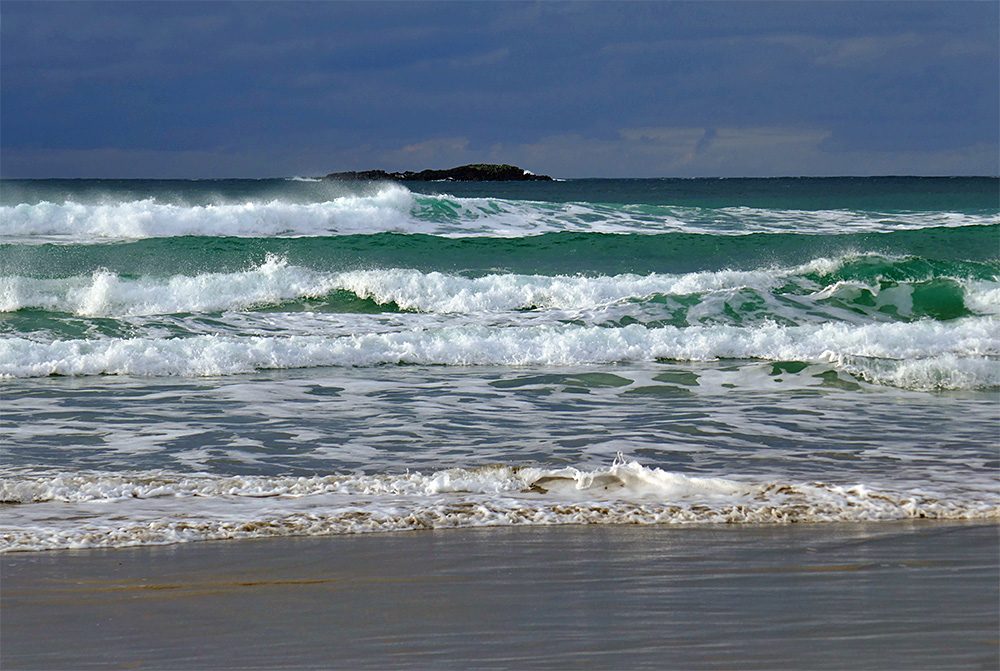 Picture of breaking waves reaching a beach, a small rocky island in the background