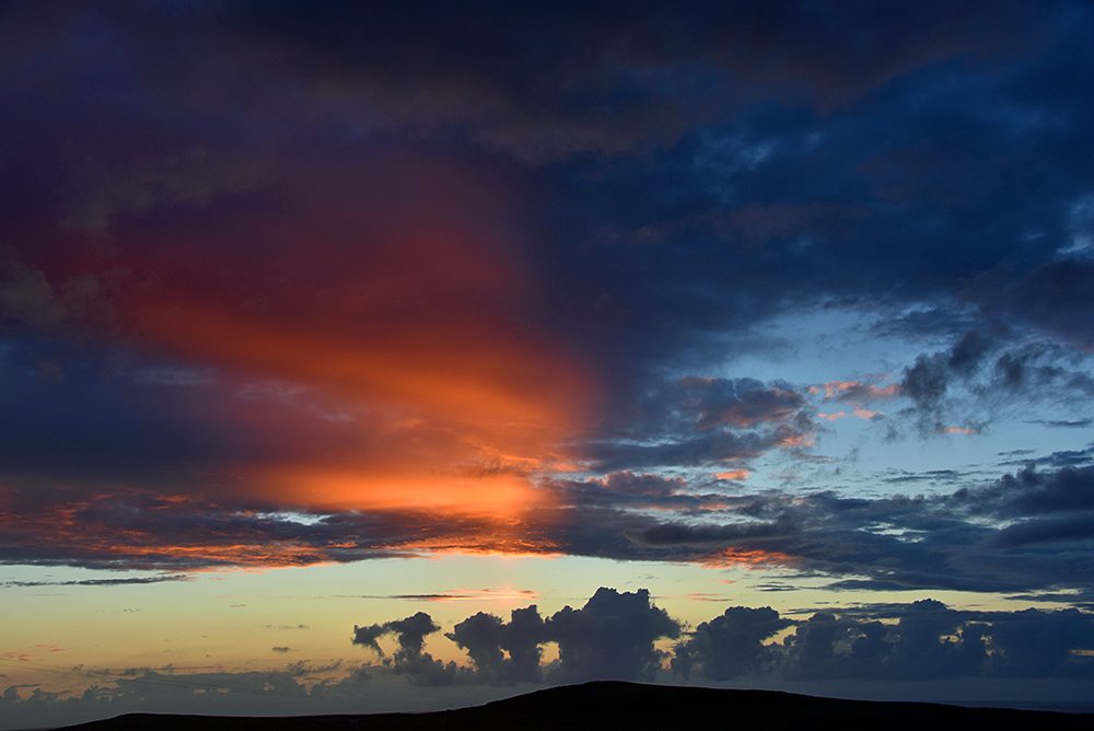 Picture of a colourful partially cloudy sunset behind a hill
