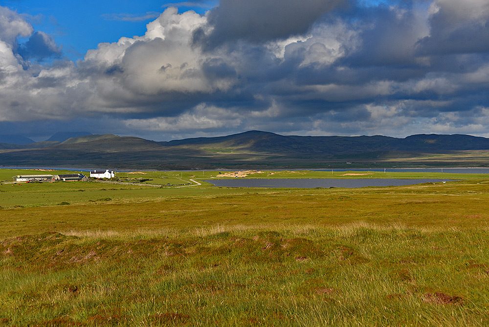 Picture of an island farm next to a small freshwater loch, a sea loch in the background