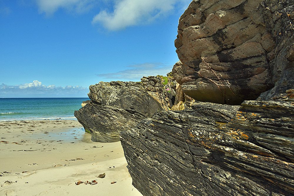 Picture of low cliffs next to a sandy beach on a bright sunny day