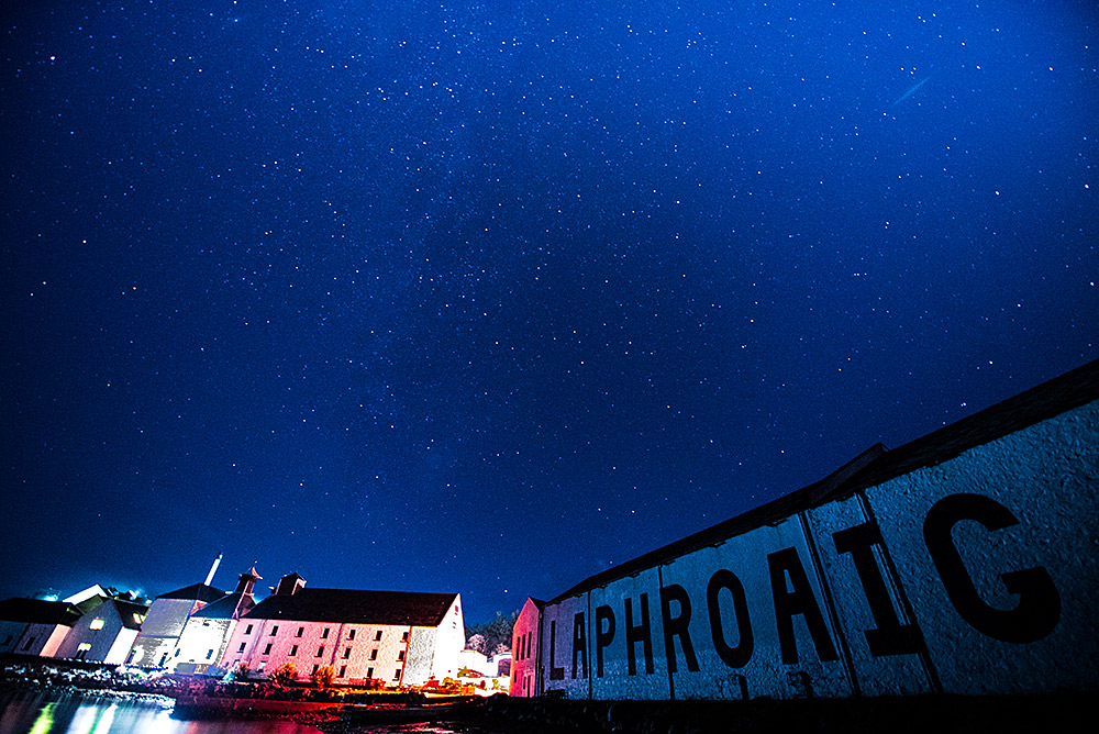 Picture of a starry night sky over a coastal distillery (Laphroaig on Islay)