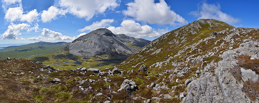 Panoramic picture from the flank of a hill, looking up to the summit and out over other hills and mountains
