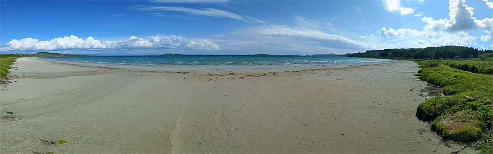 Panoramic picture over a wide sandy beach at a large bay with some small islands