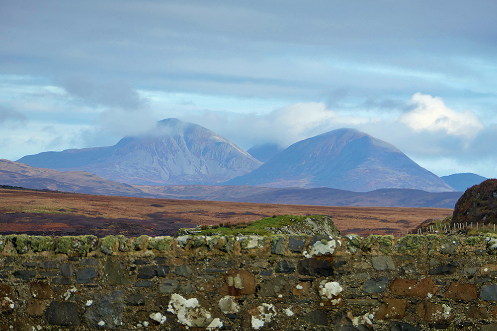 Picture of three mountains behind an old stone wall