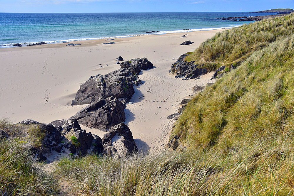 Picture of a view over a beach with some rocks, seen from a row of dunes