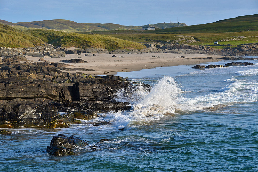 Picture of a coastal landscape with rocks, waves splashing over rocks, beach and dunes