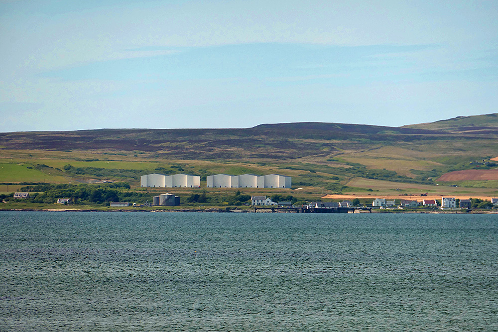 Picture of two distillery maturation warehouses on a hillside, seen across a sea loch