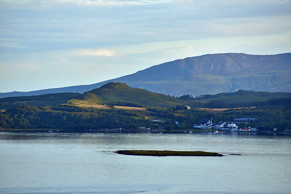 Picture of a small coastal village with a hotel and a distillery seen from a hill across the bay